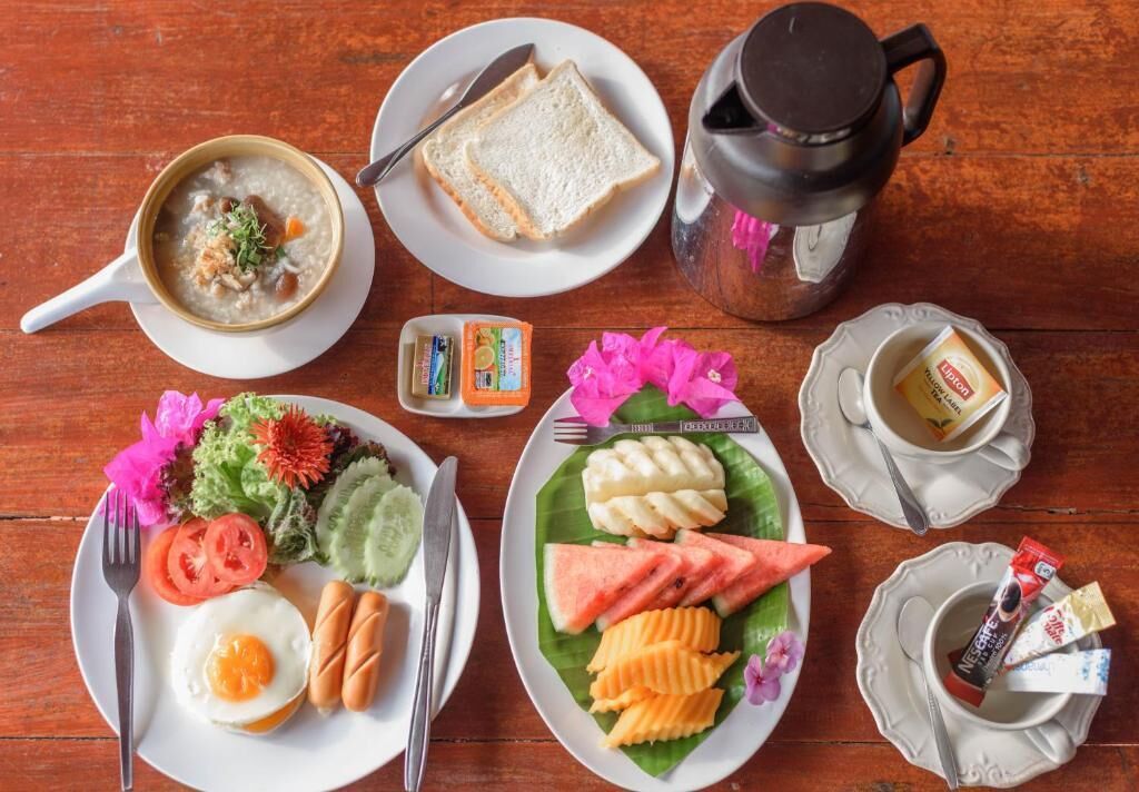 A breakfast setting with a bowl of soup, toast, a coffee pot, a plate with eggs, sausages, and a banana split.