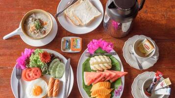 A breakfast setting with a bowl of soup, toast, a coffee pot, a plate with eggs, sausages, and a banana split.