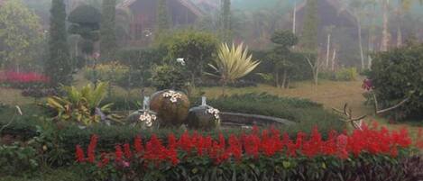 A garden with various plants and a traditional building in the background.