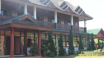 Traditional building with a multi-tiered balcony and large windows, set amidst well-maintained greenery.