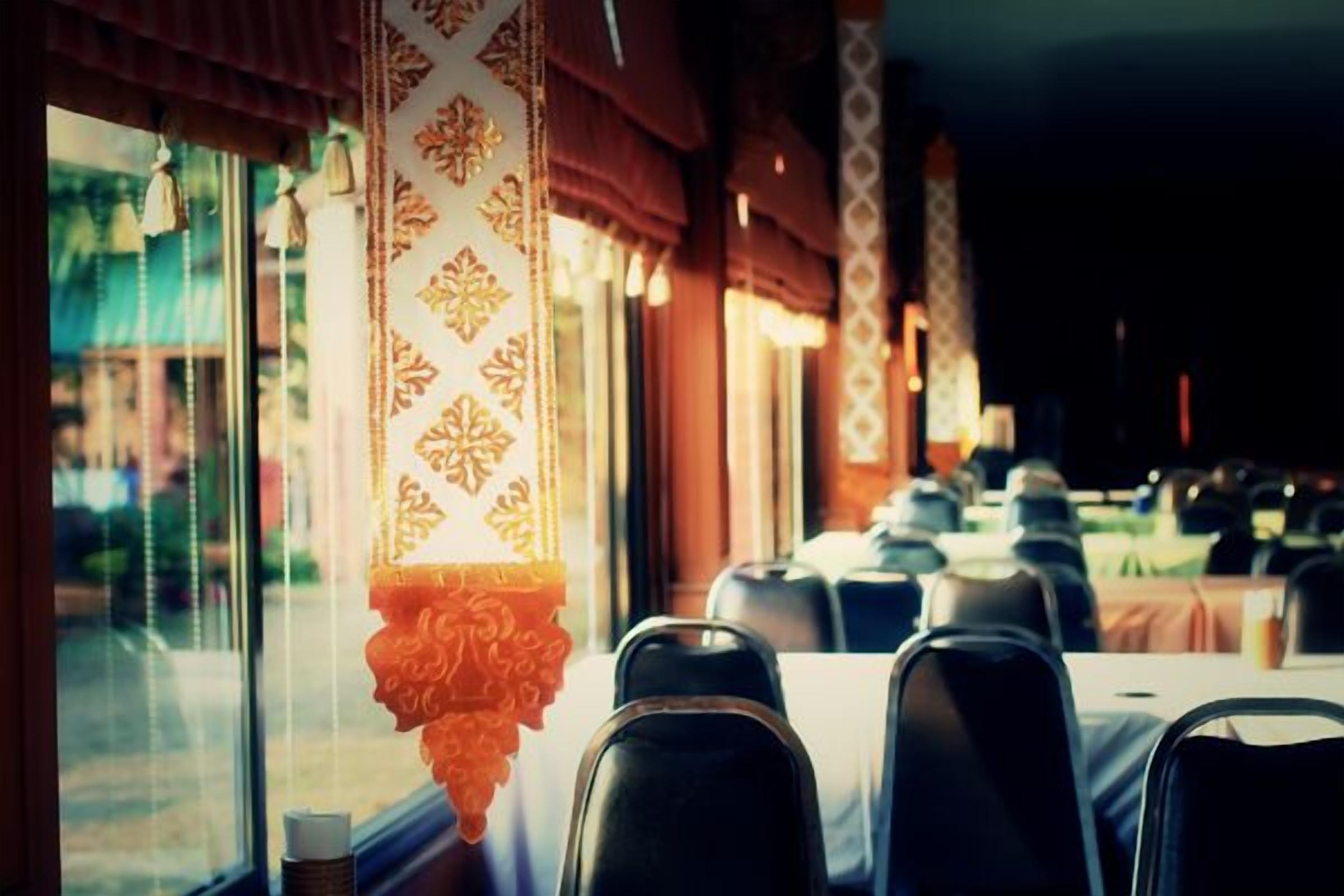 A restaurant interior with tables and chairs, patterned curtains, and a view of the outside.