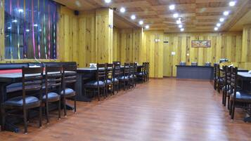 A restaurant with wooden walls and a long counter. Tables and chairs are arranged for dining.