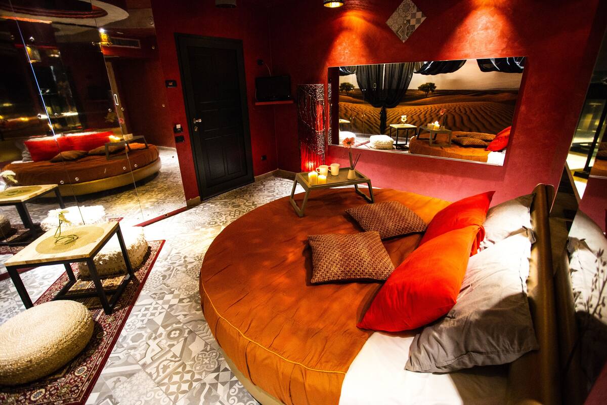 A circular bed with a wooden frame, red and white pillows, and a small table with candles.