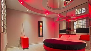 A modern bedroom with a circular bed, red accents, and a large mirror.