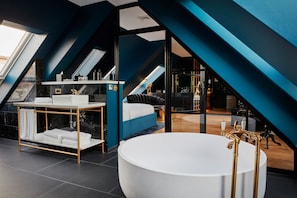A modern bathroom with a freestanding bathtub, a vanity with gold fixtures, and a bed in the background. - Provocateur, Berlin, a part of Sircle Collection (Berlin)