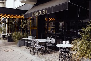An outdoor cafe area with tables and chairs, a black awning with the word "PROVOCATEUR" on it, and potted plants. - Provocateur, Berlin, a part of Sircle Collection (Berlin)