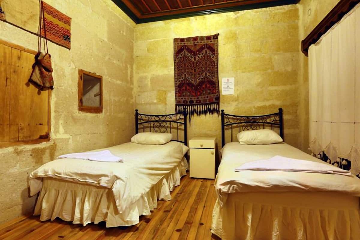 A room with two beds, wooden flooring, a tapestry, and a small cabinet.