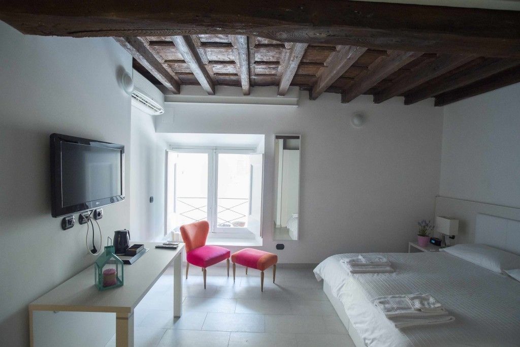 A hotel room with a bed, a desk with a TV, a chair, and a window.