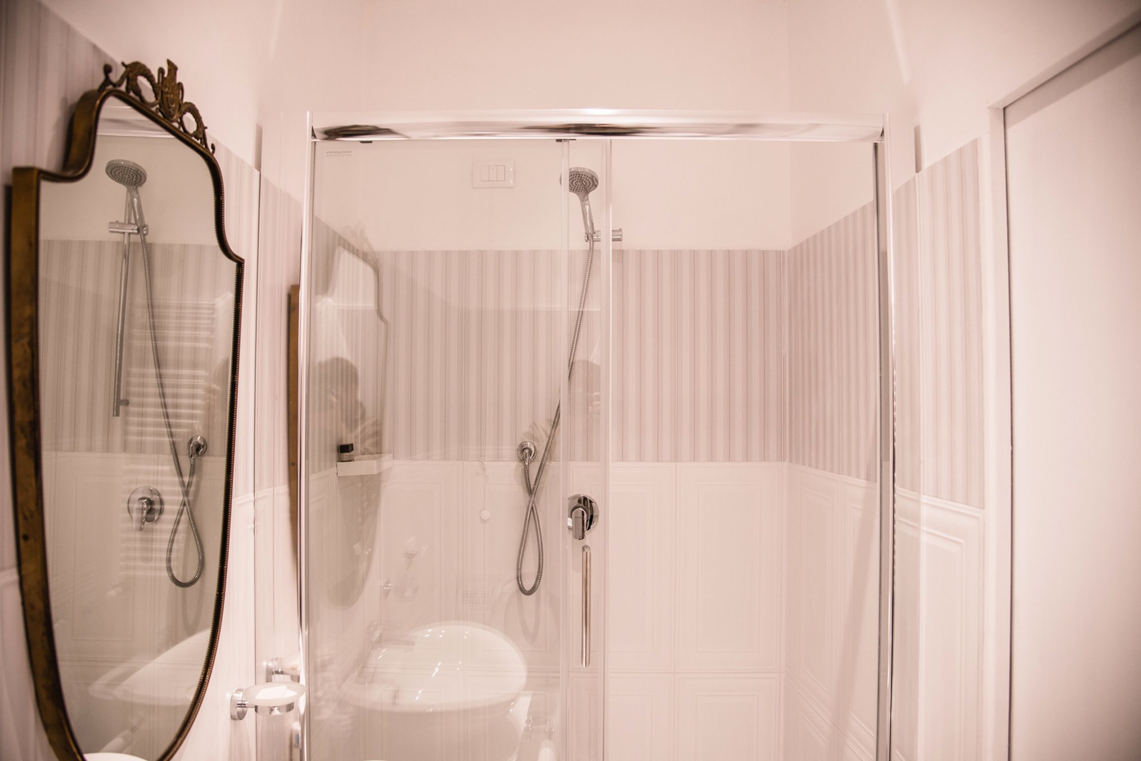 Un baño con ducha de vidrio, un lavamanos blanco y un espejo con marco decorativo.