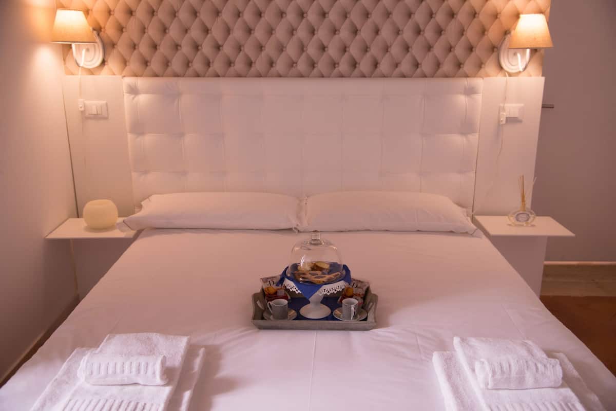 A hotel room with a large bed, two bedside tables, a decorative headboard, and a tray with snacks and drinks.