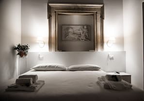 Een hotelkamer met een groot bed, twee nachtkastjes, een kunstwerk aan de muur en twee wandlampen.