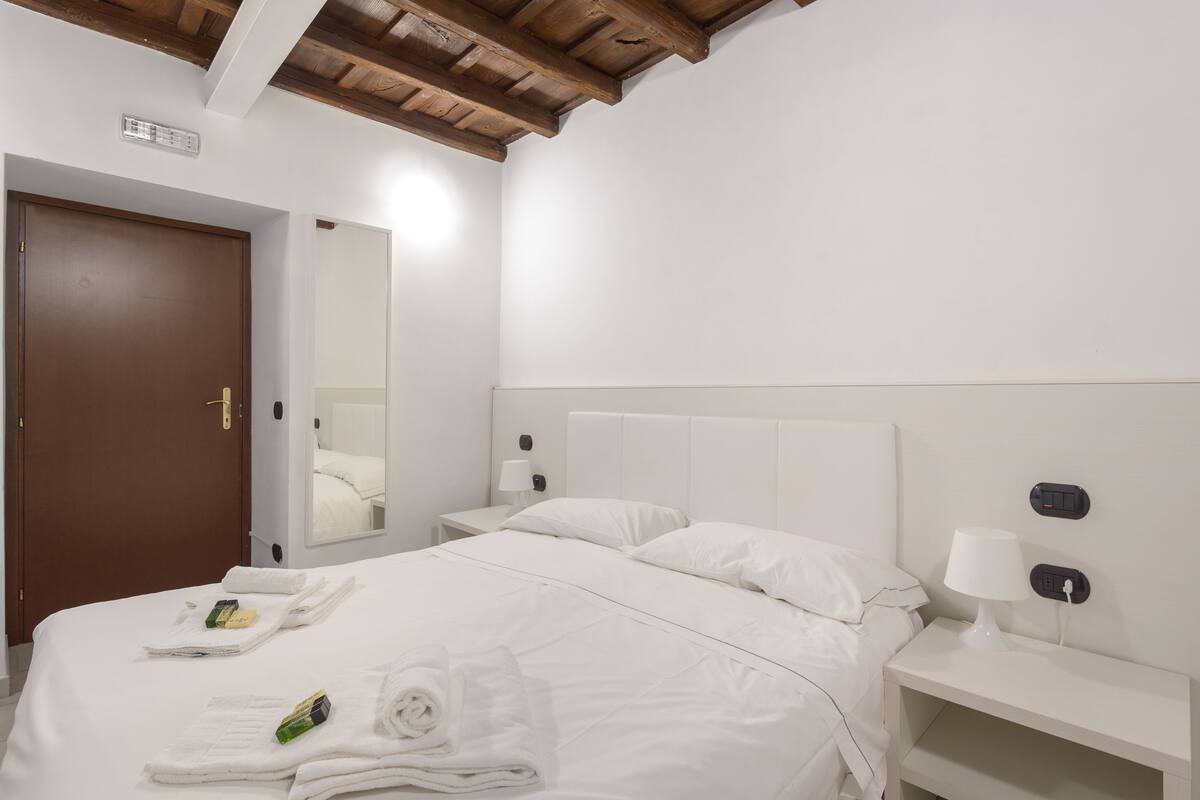 A hotel room with a large bed, a nightstand with a lamp, a wooden ceiling, and a door.