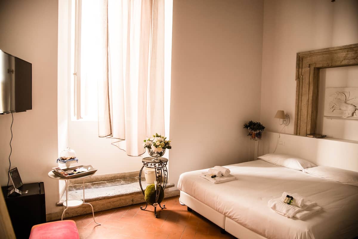 A hotel room with a bed, a desk with a lamp, a TV, and a window with curtains.