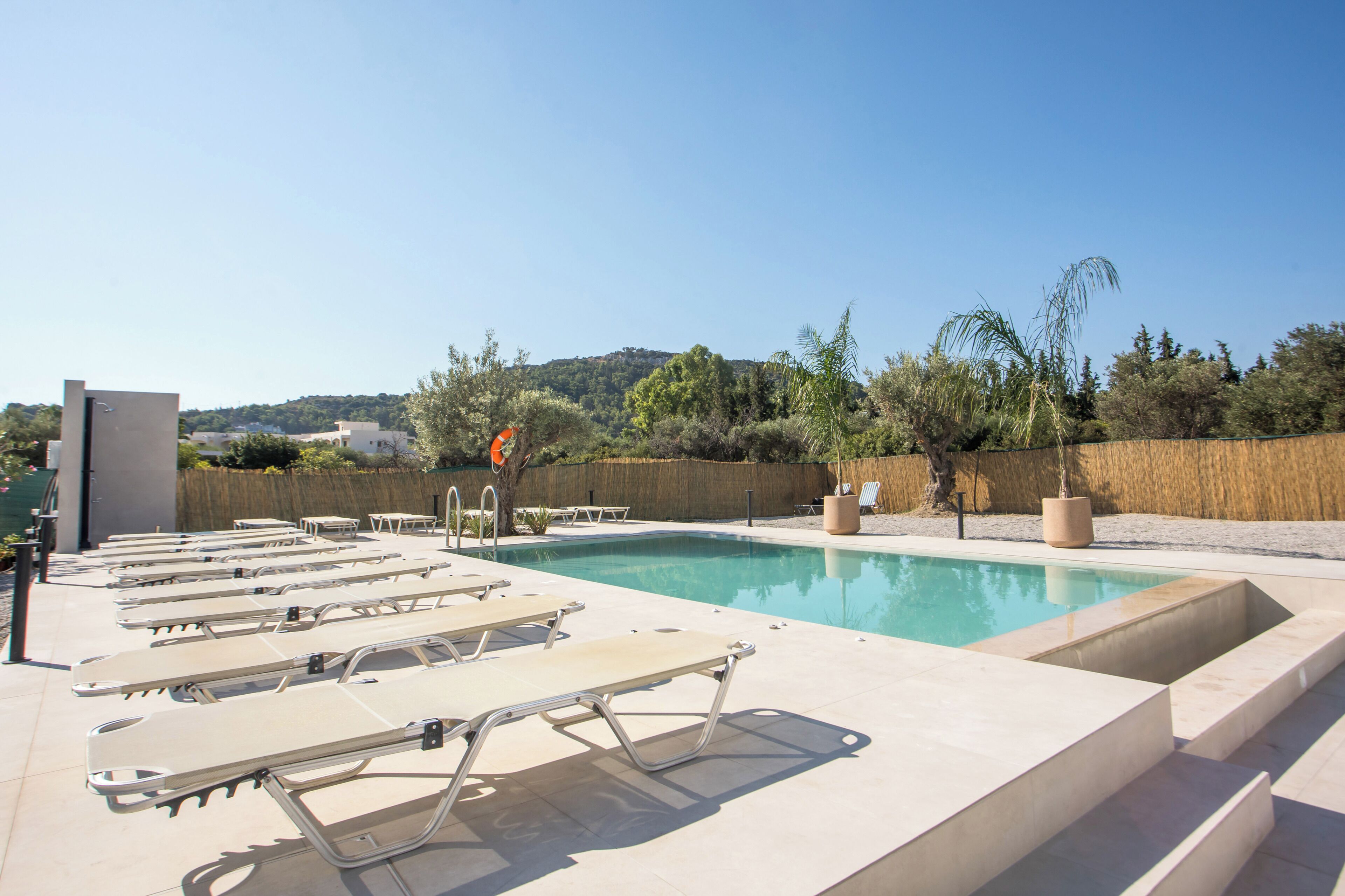 Une piscine dotée de chaises longues et d’une bouée de sauvetage, entourée d’une clôture en bois et d’arbres.