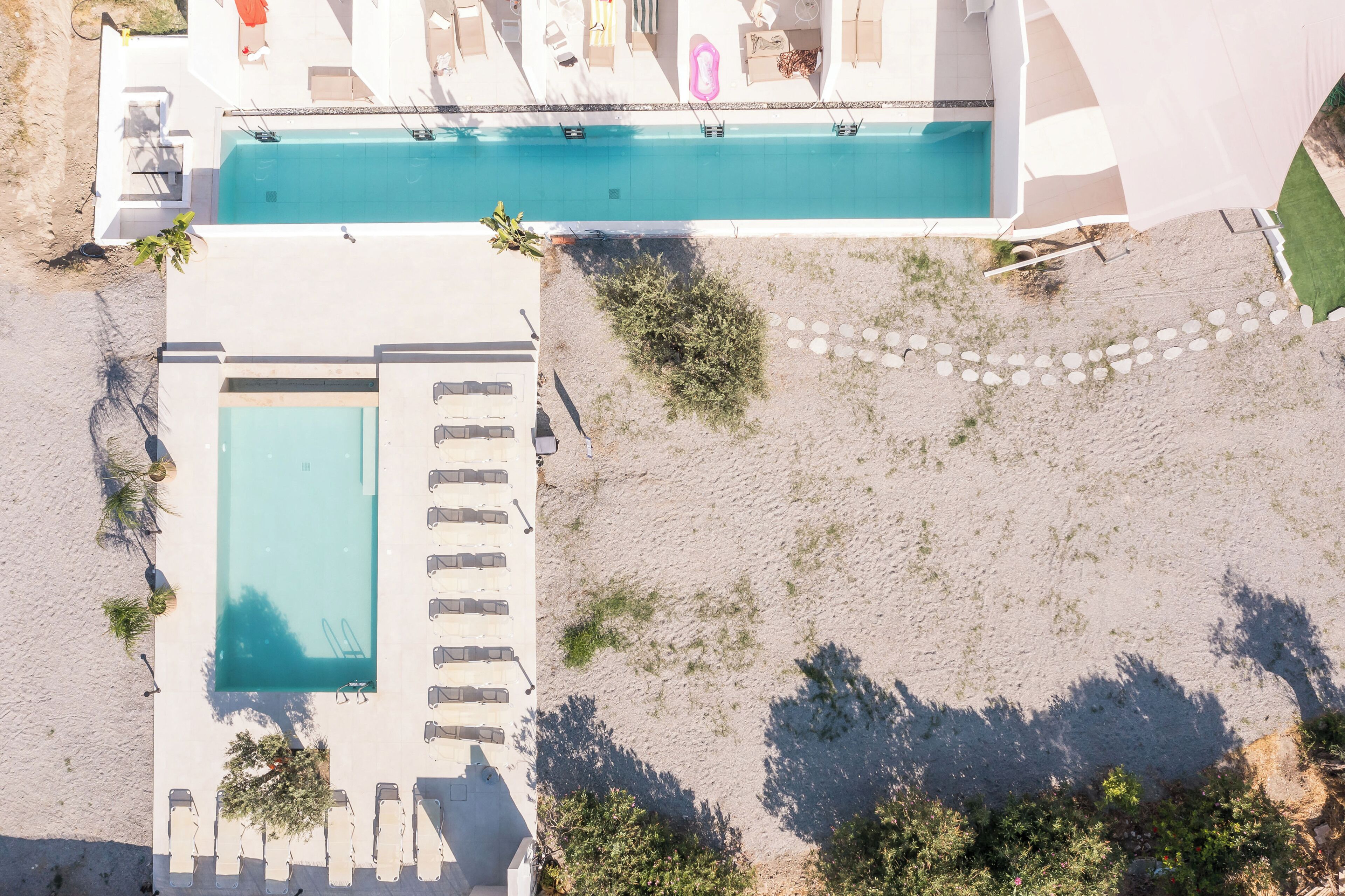 An aerial view of a hotel with a swimming pool, lounge chairs, and a landscaped area.