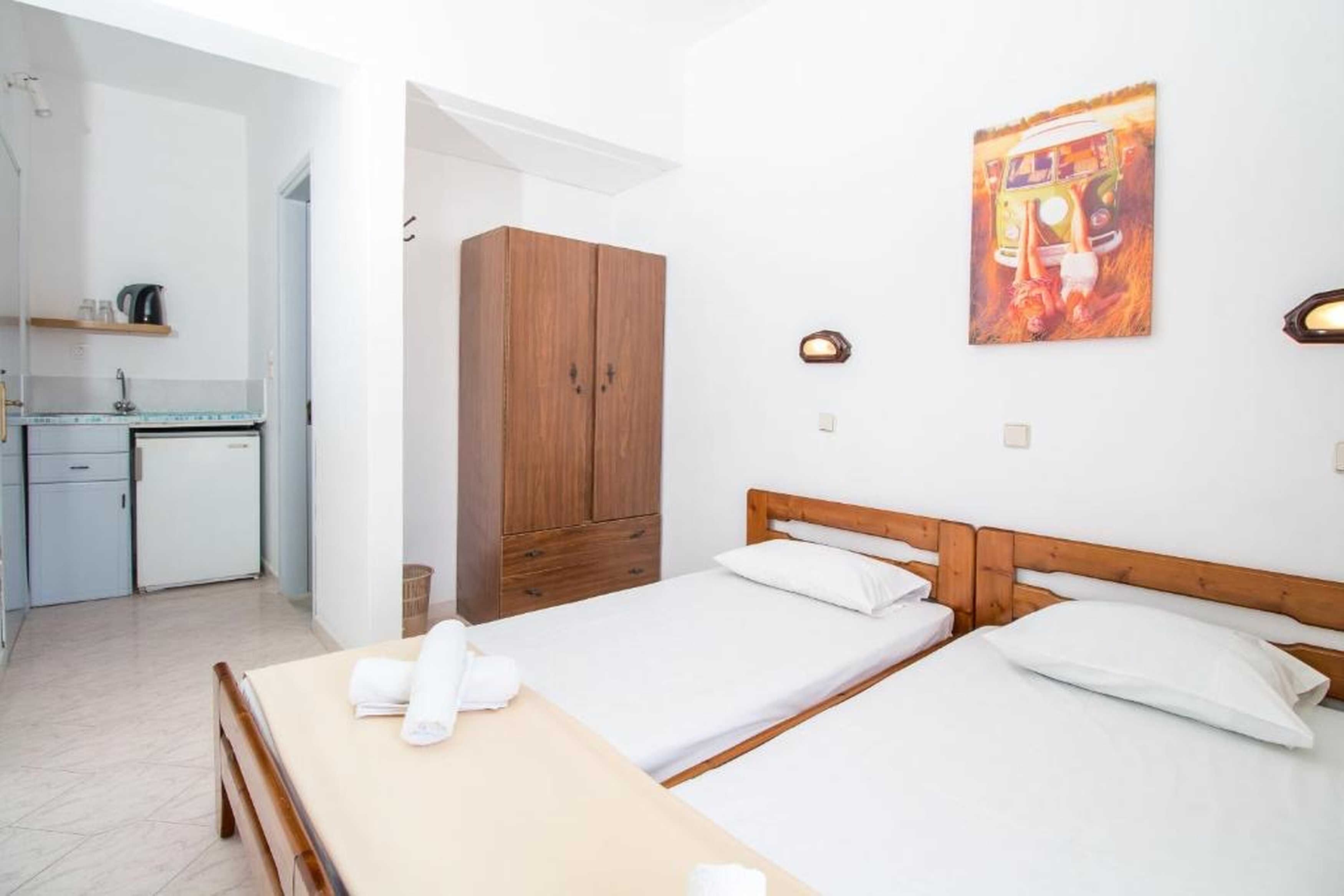 Quarto com duas camas, um guarda-roupa de madeira, uma pequena cozinha e um quadro na parede.