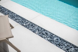 A poolside area with a white tiled deck, a small seating area, and a pebble-lined pathway leading to the pool. - Nikos BnB (Rhodes)