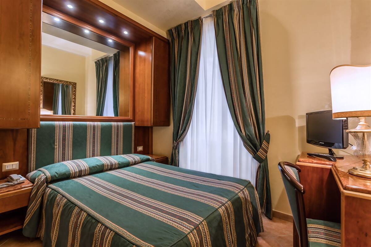 Una camera d'albergo con un letto grande, una scrivania con un computer, un telefono e uno specchio.