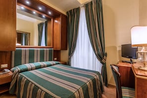 Ein Hotelzimmer mit einem großen Bett, einem Schreibtisch mit Computer, einem Telefon und einem Spiegel.