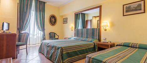 Een hotelkamer met twee bedden, een bureau met een computer, een stoel en een raam met gordijnen.