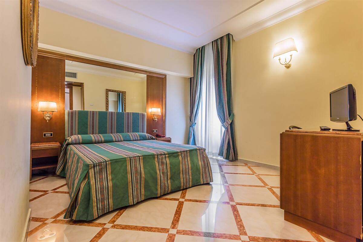 Una camera d'albergo con un letto, una scrivania in legno, una televisione e uno specchio.