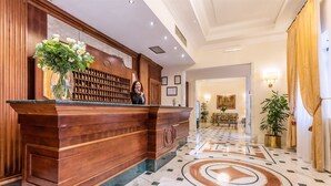 A reception desk with a wooden finish, a vase of flowers, and a framed picture on the wall. - Raeli Hotel Noto (Rome)