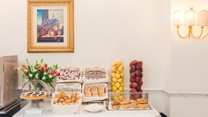 A buffet table with various food items, a framed painting, and wall-mounted lights. - Raeli Hotel Noto (Rome)
