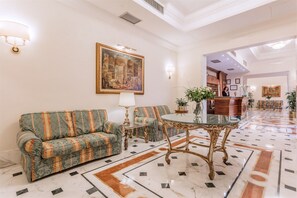 A lobby with a green sofa, a glass table, and a reception desk. - Raeli Hotel Noto (Rome)