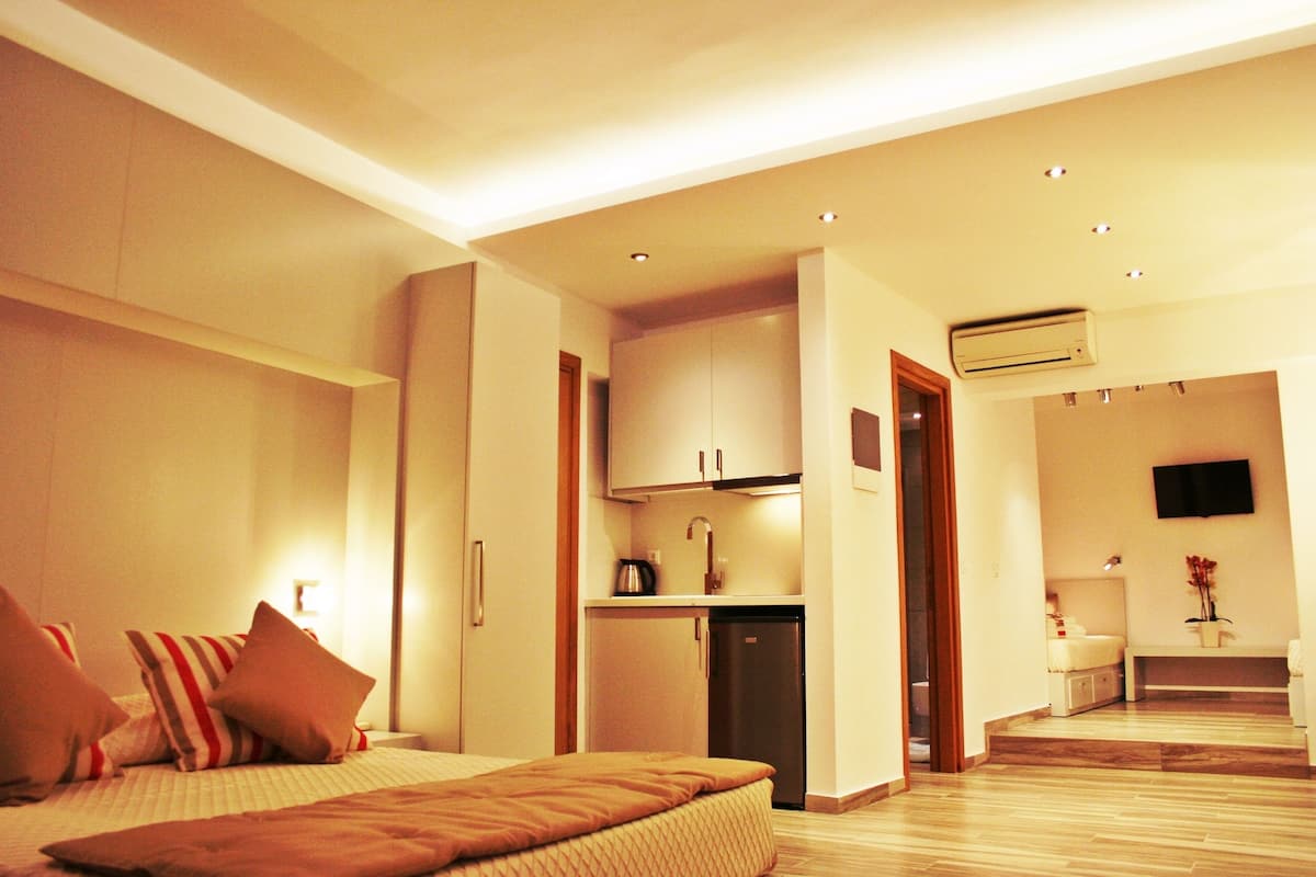 A modern hotel room with a bed, a kitchenette, and a bathroom.