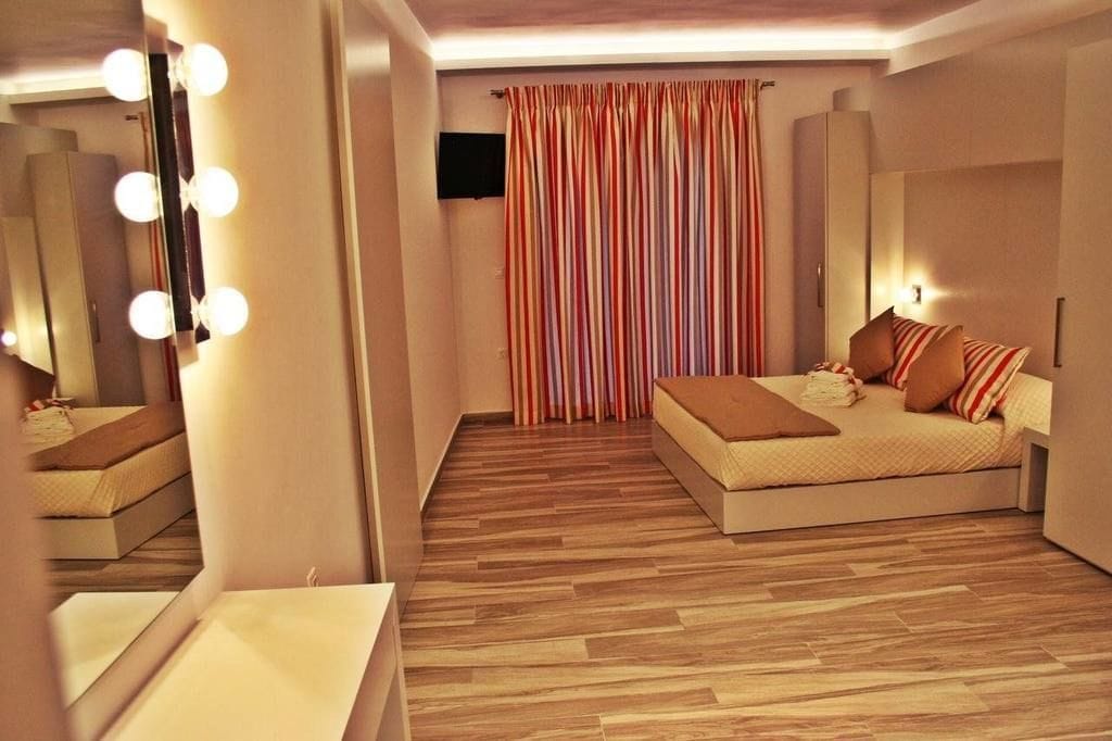 A modern bedroom with a large mirror, bedside lamps, a bed with striped bedding, and a wooden floor.