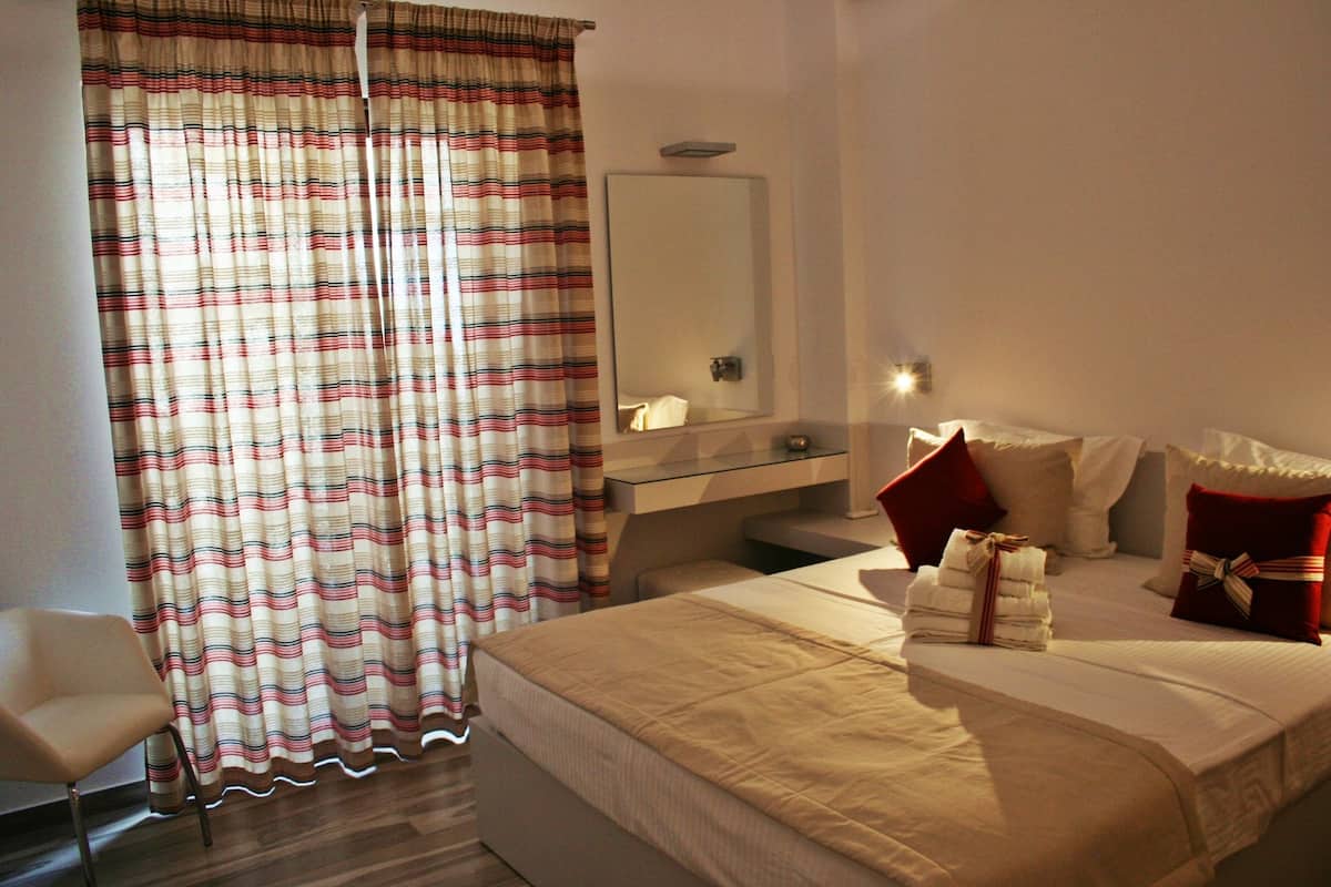 A hotel room with a bed, a chair, a mirror, and a window with curtains.