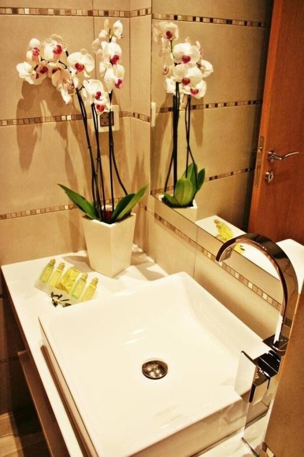 Un baño con un lavamanos blanco, un espejo y una orquídea en maceta.