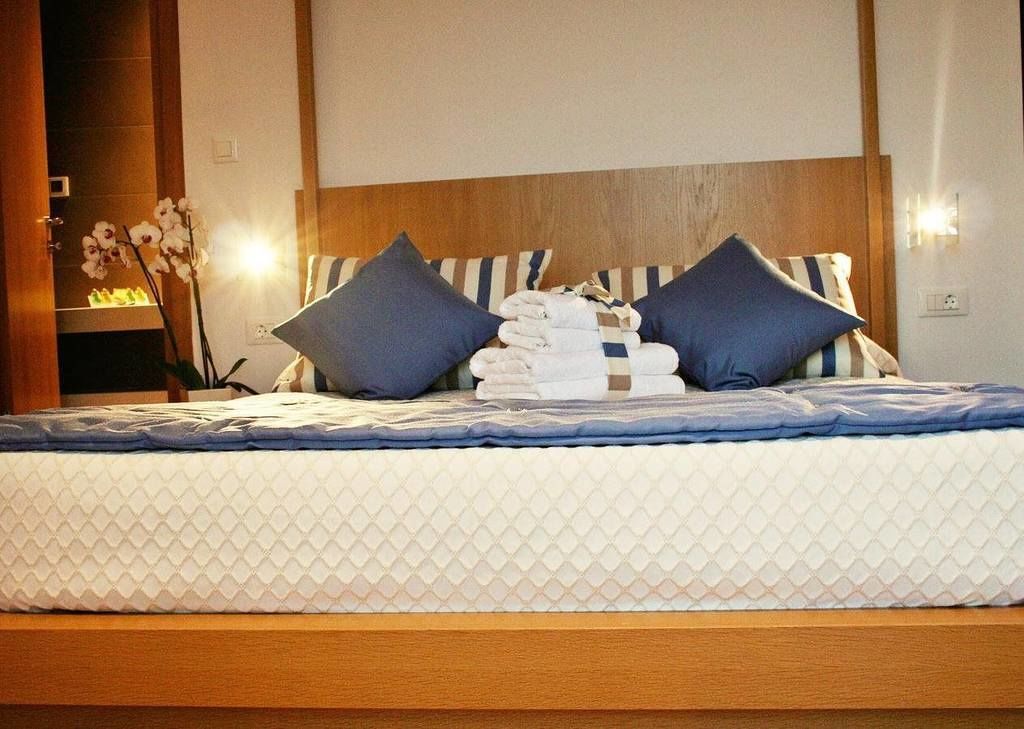 Una cama bien tendida con un cabecero a rayas, dos almohadas y una pila de toallas dobladas.