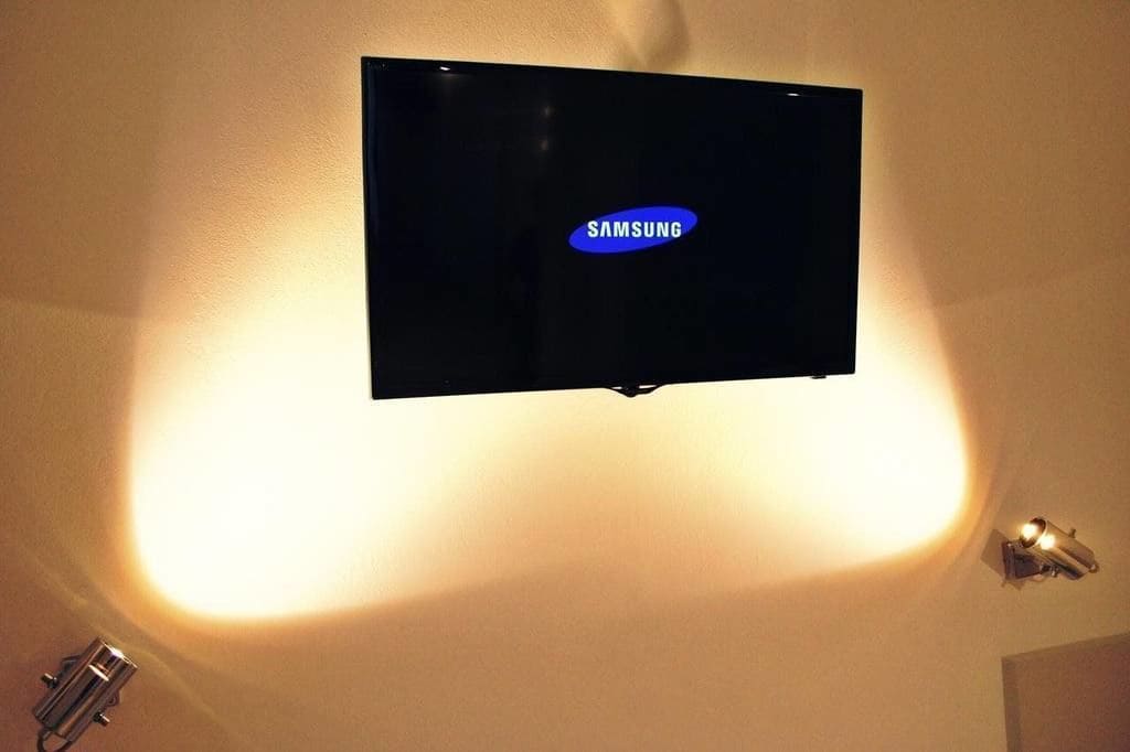 Un televisor Samsung montado en la pared, con una lámpara debajo.