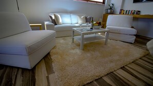 Ein modernes Wohnzimmer mit einem weißen Sofa, einem weißen Sessel, einem Couchtisch und einem flauschigen Teppich.
