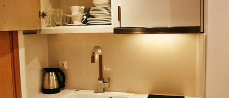 A compact kitchen with a white sink, stainless steel kettle, and an induction cooktop.
