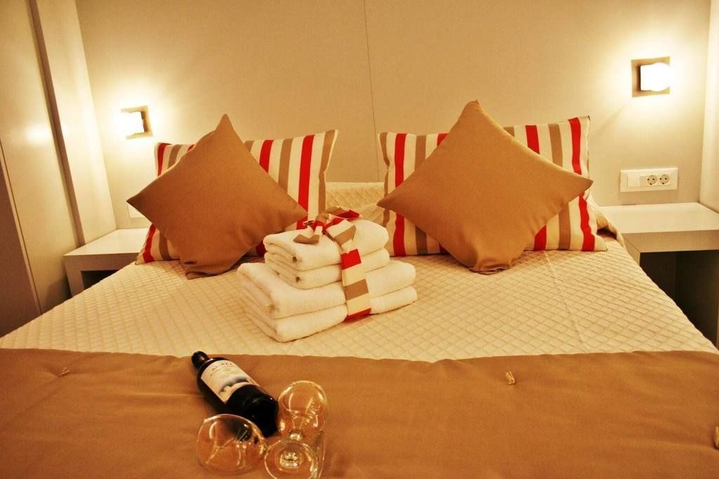 Una cama bien hecha con almohadas a rayas, una pila de toallas dobladas y una botella con vasos sobre la cama.