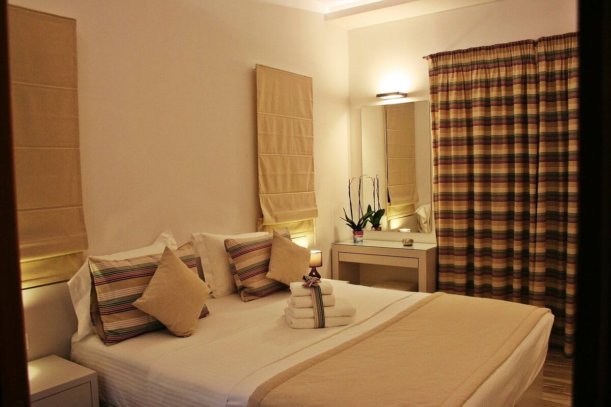 A hotel room with a large bed, bedside tables, a mirror, and a window with curtains.