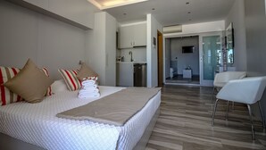 Ein modernes Hotelzimmer mit einem großen Bett, einer kleinen Küchenzeile, einem Badezimmer mit Glasdusche und einer Sitzecke.