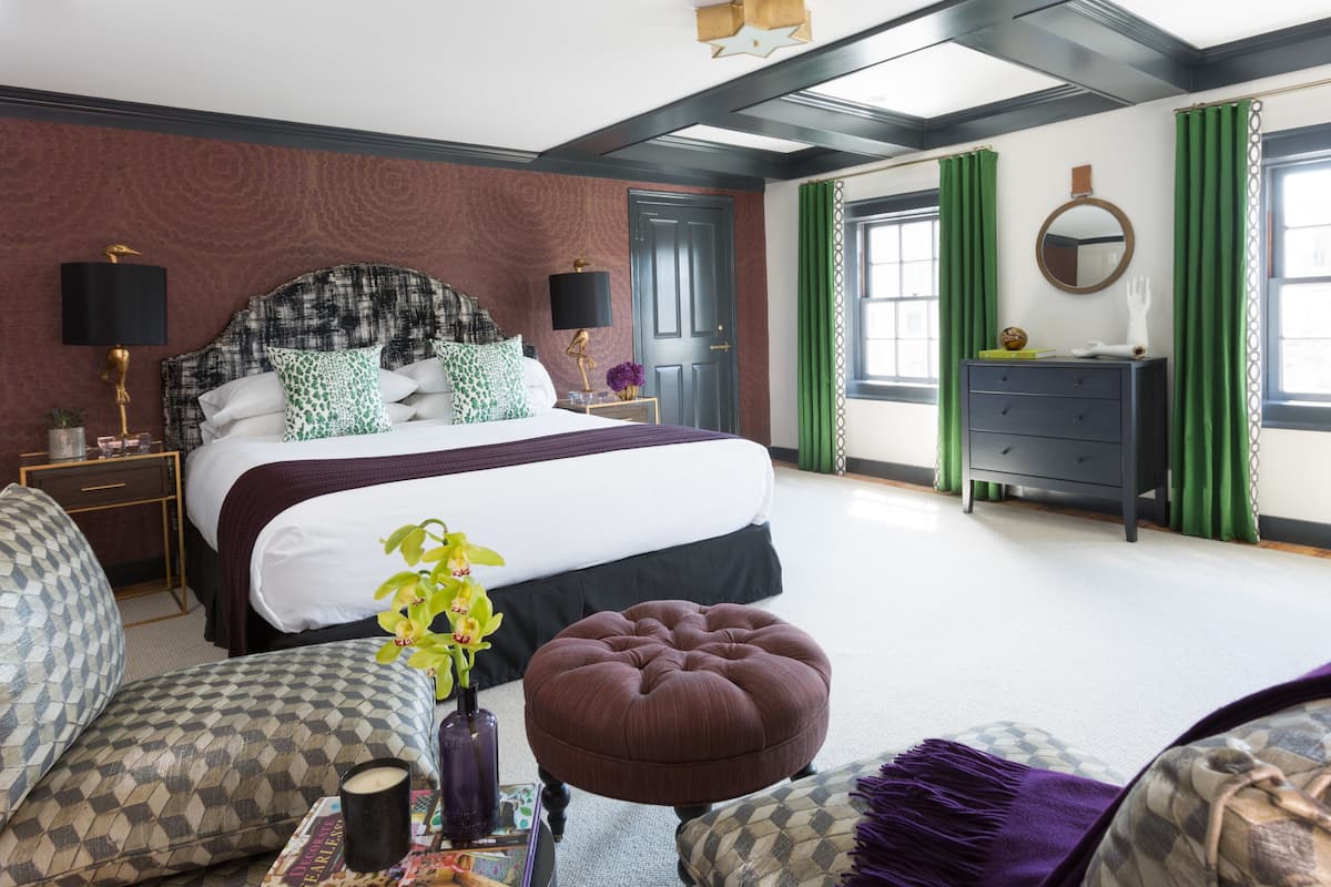 Une chambre à coucher avec un grand lit, deux tables de chevet, une commode, des rideaux verts et un miroir au mur.
