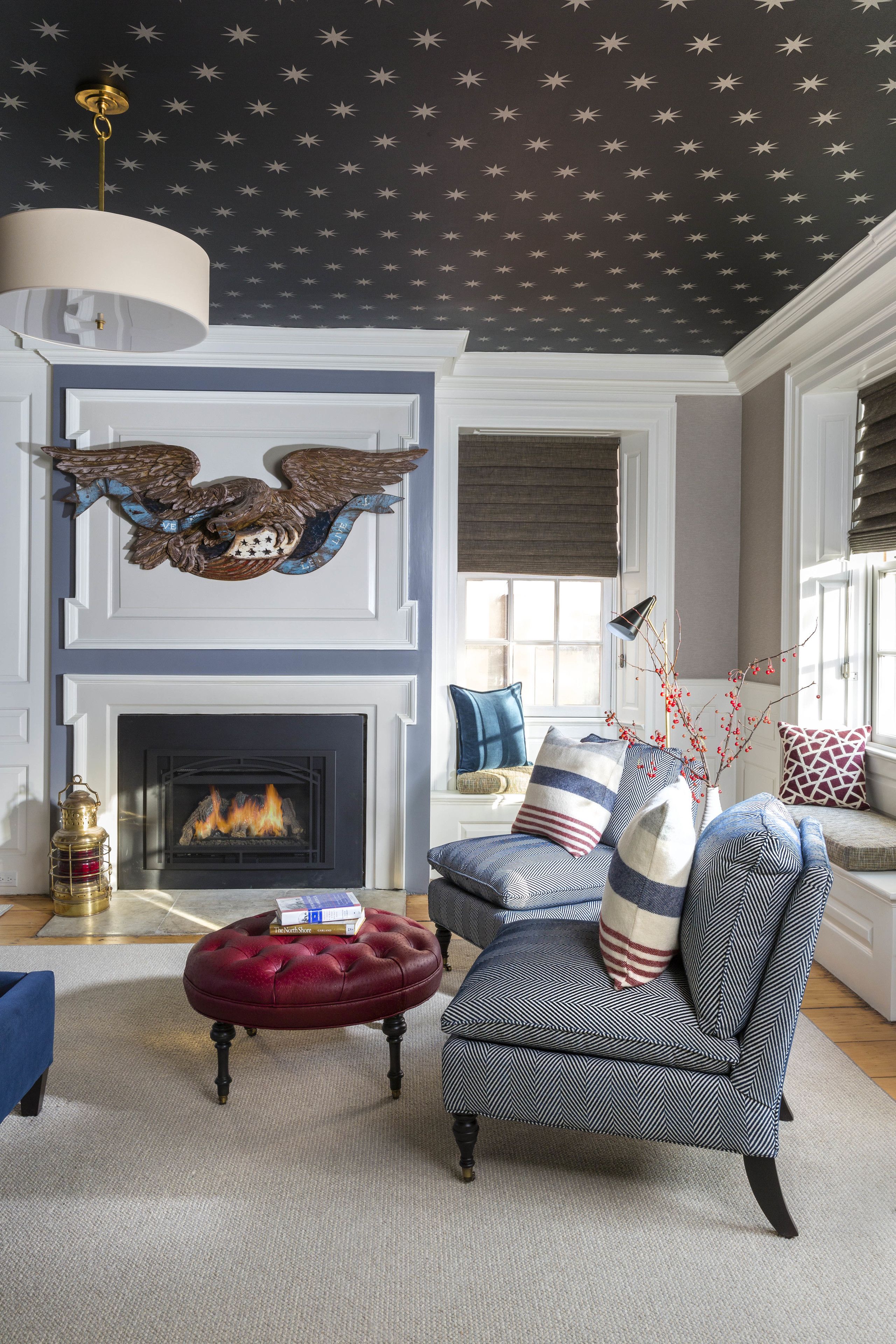 A living room with a fireplace, a red ottoman, a blue armchair, and a decorative ceiling with star patterns.