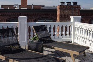 A rooftop terrace with two lounge chairs, a small table with a plant, and a white balustrade.