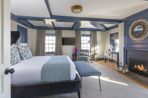 A bedroom with a large bed, a fireplace, a television, and a window with curtains.