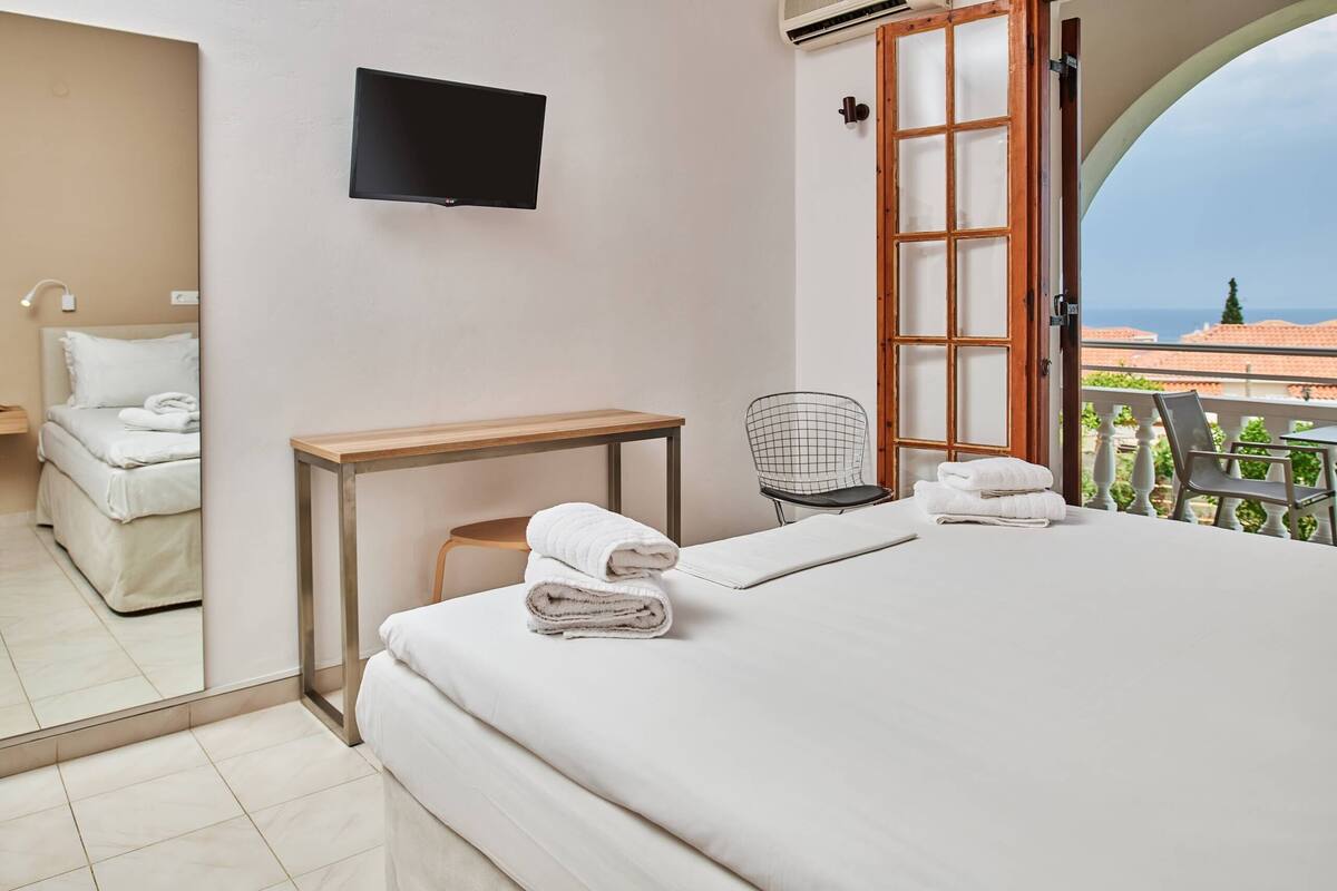 Une chambre d’hôtel avec un lit, un téléviseur fixé au mur, une petite table, une chaise et un balcon avec vue.