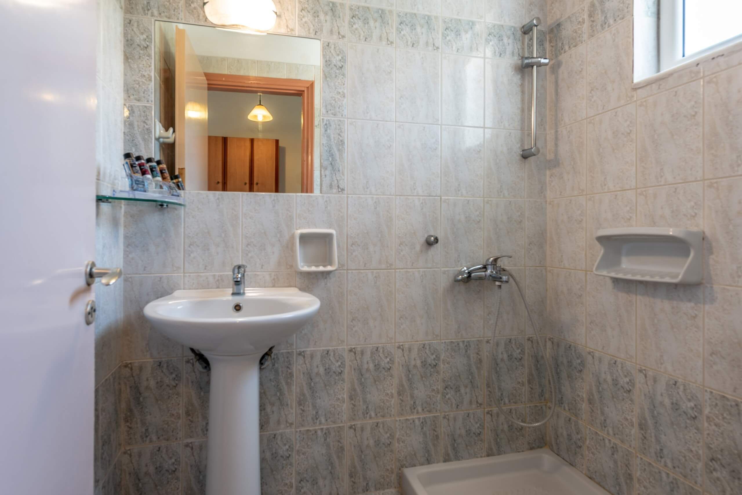 Ein Badezimmer mit einem Standwaschbecken, einer Handbrause und einem kleinen Fenster.