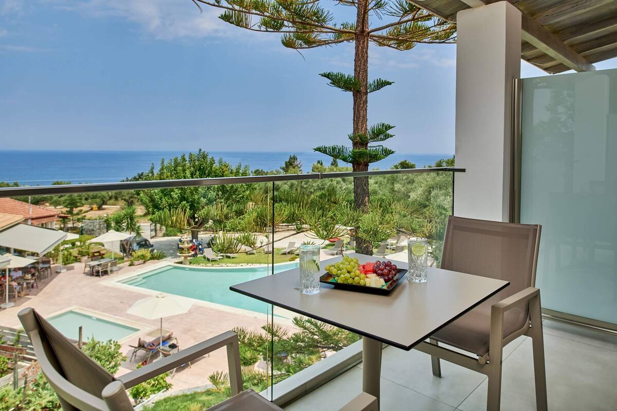 Un balcon avec une table dressée pour deux personnes, donnant sur une piscine et une végétation luxuriante.