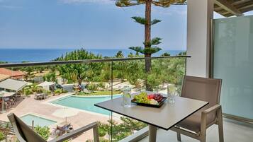 A balcony with a table set for two, overlooking a pool and lush greenery.