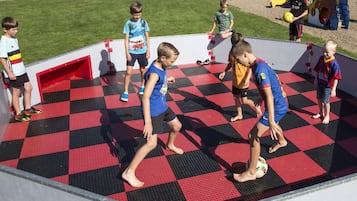 Een groep kinderen speelt op een schaakbordvloer met een rood en zwart patroon.