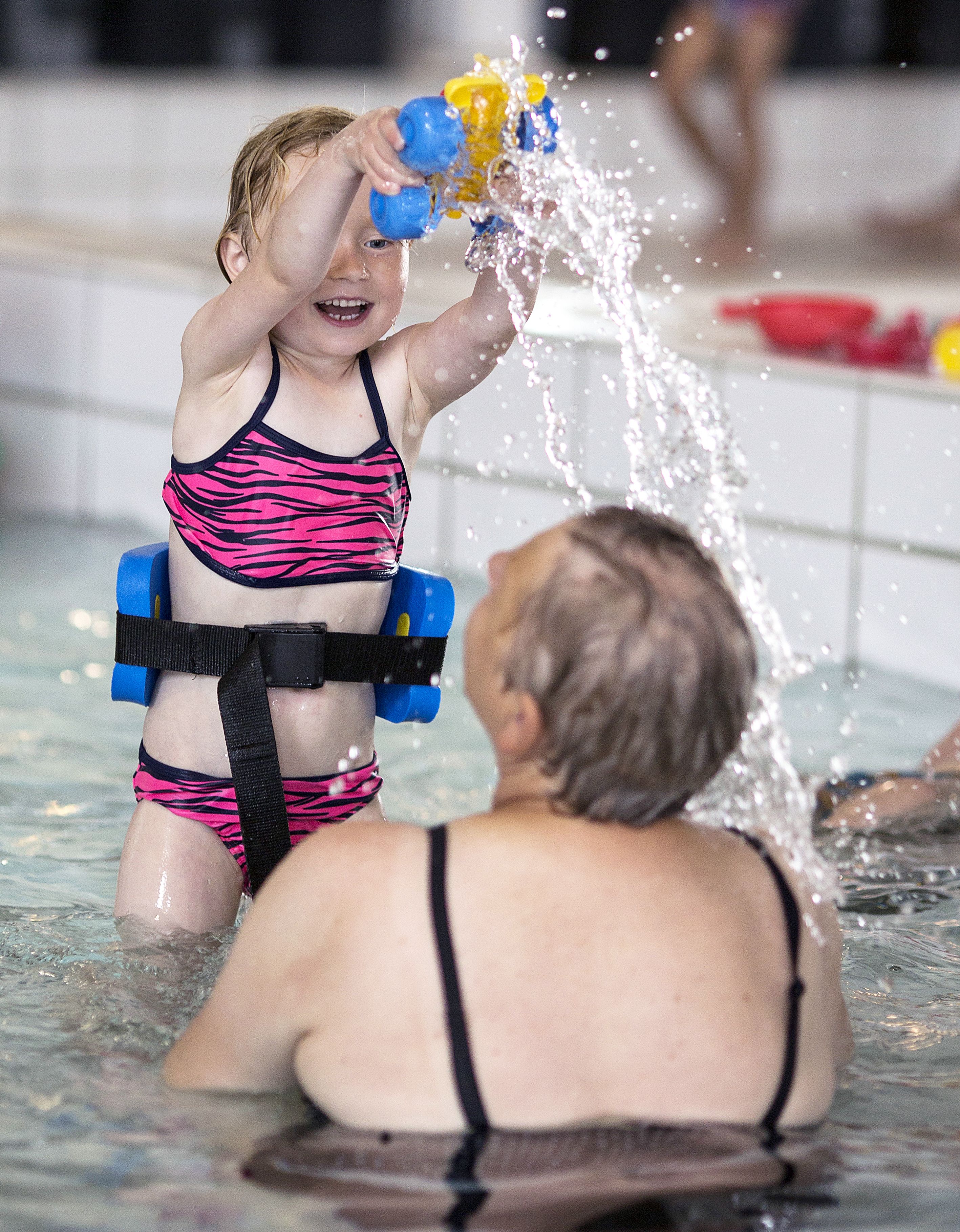 A child in a pool with an adult, both wearing swimwear.