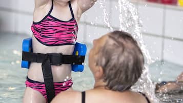 A child in a pool with an adult, both wearing swimwear.